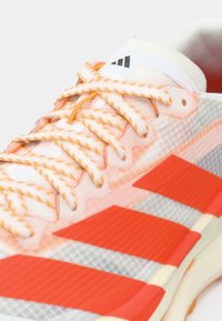 Διάφανο αθλητικό παπούτσι με πορτοκαλί λεπτομέρειες, υφασμένες γκρι και κόκκινες ρίγες και πλεκτά κορδόνια. Διαθέτει επενδεδυμένη γλώσσα και ετικέτα με λογότυπο.