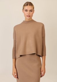 Strickpullover in Hellbraun, mit einem hohen Rippkragen und dreiviertellangen Rippärmeln. Das Design ist kastig mit einem geschichteten vorderen Saum.