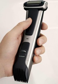 Rasoir électrique avec un corps en acier inoxydable, des accents en caoutchouc noir et une prise texturée. Il dispose d'une tête de coupe argentée et d'un bouton de réglage.
