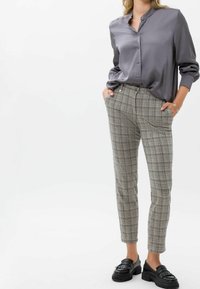 Blusa in satin grigia con chiusura a bottoni, abbinata a pantaloni a quadri su misura in tonalità di grigio e nero, completata da mocassini neri.