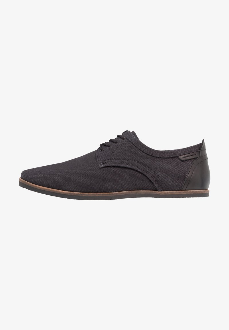 Chaussure décontractée noire à lacets avec dessus en toile et accent cuir au talon, avec une semelle fine marron et un design épuré.