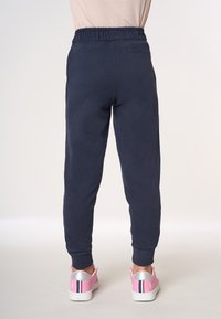 Pantaloni della tuta blu navy con vita elastica e polsini a coste, dotati di una tasca posteriore. Indossati con sneakers rosa e suole bianche.
