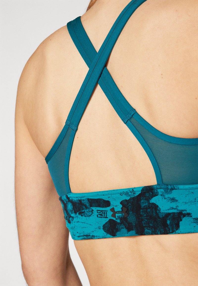 Reggiseno sportivo turchese con una fascia testurizzata che presenta un design astratto nero, spalline incrociate dettagliate e una finitura in tessuto liscia.