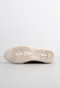 Shoe sole in light beige with textured rubber grip, featuring a zigzag pattern and logo. The design is flat with an even surface.