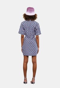 Vestito camicia a maniche corte di colore blu navy con motivo geometrico rosa e bianco, stretto in vita; abbinato a un cappello a secchiello viola chiaro.
