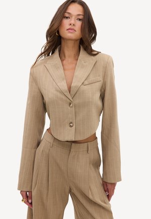 Femme portant un blazer court beige à fines rayures avec deux boutons et un pantalon large plissé taille haute assorti.