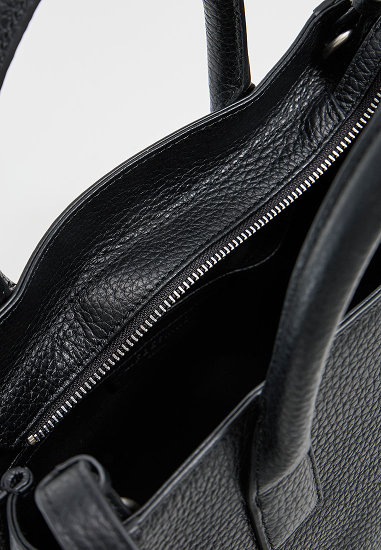 Schwarze, strukturierte Lederhandtasche mit zwei Griffen und einem teilweise offenen silbernen Reißverschluss, der das Innenfutter zeigt.