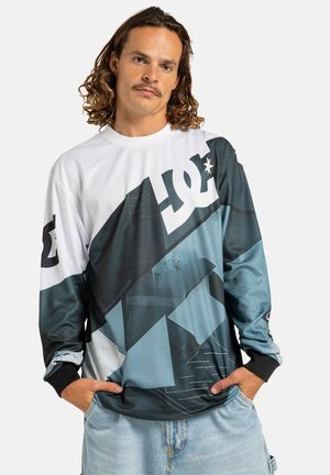 Camisa gráfica de manga larga hecha de poliéster. Presenta un diseño geométrico en tonos de azul y negro con un gran logo blanco en el pecho.