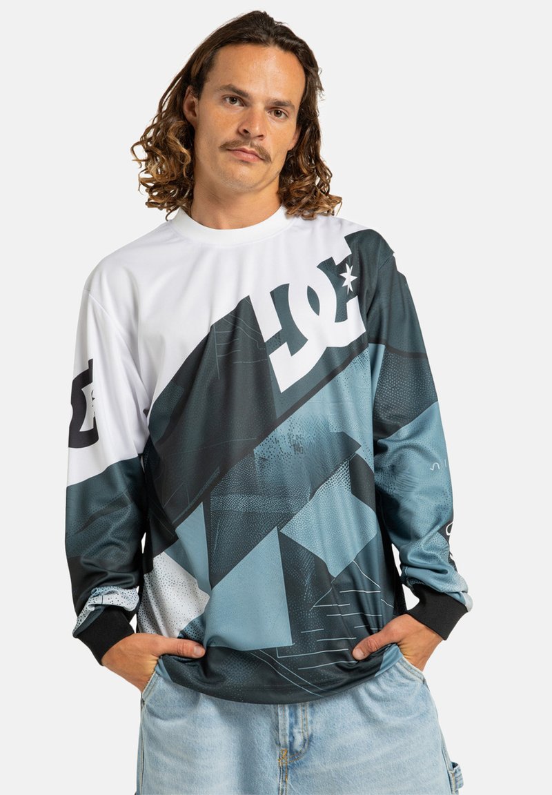 Košeľa s dlhým rukávom, vyrobená z polyesteru. Obsahuje geometrický výkon v odtieňoch modrej a čiernej s veľkým bielym logom na hrudi.