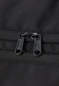 Black fabric bag with two zippered closures featuring black zipper pulls. Textured surface with stitching detail along the seams.