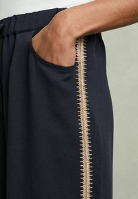 Marina joggerbyxor med sidficka och en distinkt beige zigzagstickning längs fickans söm. Mjuk textur.