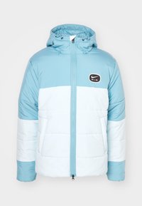 Ljust blå pufferjacka med huva och ett vitt horisontellt rand, framzipper och "Nike Air"-logotyp på vänster bröst. Slät tygtextur.