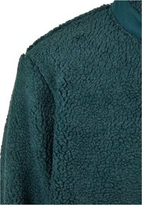 Tessuto in pile verde teal morbido con una superficie testurizzata. Presenta un collo rotondo e un materiale soffice e accogliente, ideale per calore e comfort.