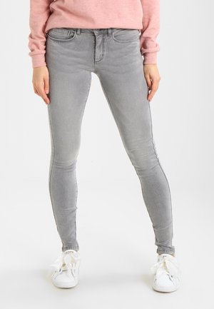 Jean skinny gris à texture lisse, avec une taille mi-haute et un design classique à cinq poches, associé à des baskets blanches.