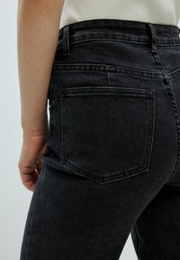 Schwarze Jeans aus Denim mit hohem Bund und Gesäßtaschen, ausgestattet mit einer glatten Textur und robusten Nähten an den Säumen.