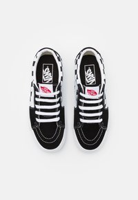 Sorte semsket sneakers med hvite snørebånd, sjakkbrikkeakenter og et mønster på kragen. Vans-logo på tungen og siden.