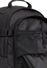 Mochila negra con un exterior de tela suave. Cuenta con un bolsillo de malla, un compartimento con cremallera, un asa resistente y un hardware de correa ajustable.
