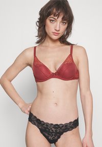 Sutiã vermelho com rendas e alças ajustáveis, com um discreto detalhe de laço no centro, combinado com cuecas bikini de rendas pretas com padrões florais.