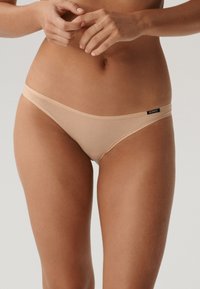 Beżowe majtki bikini wykonane z miękkiego, elastycznego materiału. Charakteryzują się minimalistycznym designem z cienką elastyczną talią i subtelnym akcentem logo.