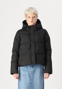 Černá péřová bunda s kapucí, prošívaný design, přední zip a elastické manžety. V kombinaci se světle modrou džínovou sukní.