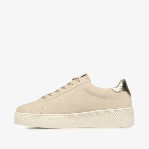 Zapatilla deportiva beige de corte bajo con suela gruesa y texturizada, lengüeta trasera metálica dorada y cordones dorados a juego sobre un fondo blanco.