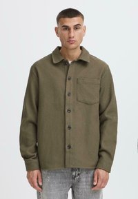 Olive green textured jacket with a collar, front buttons, and a chest pocket. Long sleeves with cuffs and a relaxed fit.