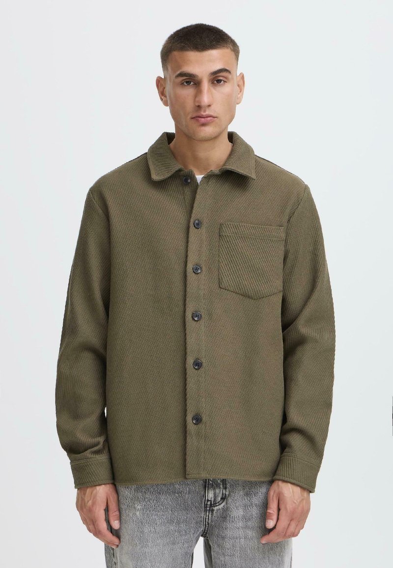 Olive green textured jacket with a collar, front buttons, and a chest pocket. Long sleeves with cuffs and a relaxed fit.
