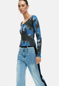 Pikad varrukadega pluus musta ja sinise triibulise mustriga, millel on kausskrae ja tekstuuritud viimistlus. Sobitatud helepesuga teksapükstega.