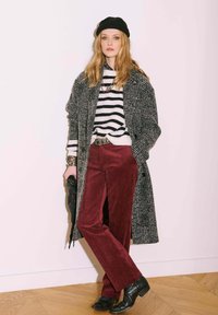 Un pull noir et blanc à rayures, un pantalon en velours côtelé bourgogne, un manteau noir et des bottes noires. Complété par un bonnet noir et des colliers superposés.