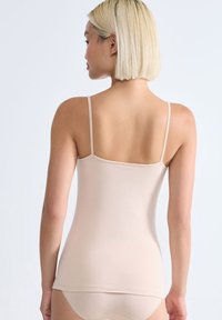 Nudý top na ramínka s úzkými pásky, vyrobený z hladkého, elastického materiálu, se přiléhavým střihem a bezešvým zadním dílem pro pohodlí.