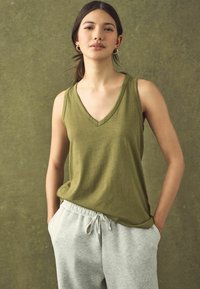 Haut sans manches en vert olive avec décolleté en V, fabriqué en tissu doux, associé à un pantalon de jogging gris clair à taille élastique avec poches latérales.