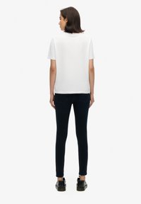 T-shirt blanc à manches courtes avec un col rond, associé à un jean skinny bleu marine et des chaussures noires à finition brillante.