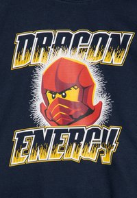 Navy blue T-shirt featuring a red helmeted character with a yellow face, surrounded by explosive white bursts, and bold text reading "DRAGON ENERGY."