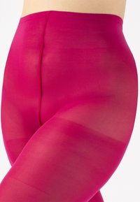 Collant fucsia senza cuciture con una texture liscia e semi-trasparente, caratterizzati da un'alta vita e una vestibilità aderente sulle gambe.