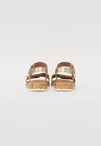 Gold-toned sandals with a cork-textured platform, featuring multiple straps and a decorative accent on the ankle strap.