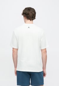 Λευκό κοντομάνικο μπλουζάκι με στρογγυλή λαιμόκοψη και μαύρο λογότ υπο Jordan στο πάνω μέρος της πλάτης. Μαλακό ύφασμα και άνετη γραμμή. Φοράται με μπλε σορτς.