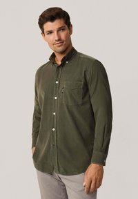 Camisa de algodón verde oliva con botones y cuello, un bolsillo en el pecho y botones blancos. Presenta mangas largas y un corte relajado.