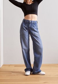 Ljust blå högmidjade jeansbyxor med rak bendesign. Har framfickor och knäppning. Slät textur.