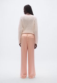 Pull tricoté rose clair à coupe décontractée, associé à un pantalon rose pastel fluide à jambes larges avec une ceinture élastique et une poche arrière.