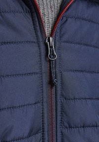 Navy puffer jacket featuring quilted texture, full front zipper with red accents, and a grey knitted interior layer visible at the collar.