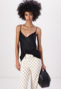 Črna satenska majica s tankimi naramnicami, v kombinaciji s kremnimi hlačami z vzorcem, ki vsebuje geometrijski dizajn, ter oblačenjem črne torbice.