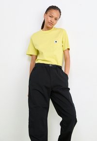 Gelbes Baumwoll-T-Shirt mit einer Brusttasche, kombiniert mit schwarzen, tapered Hosen mit Gürtel und Seitentaschen. Schlichtes Design, lässige Passform.