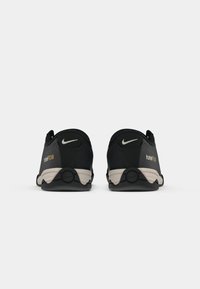Par nogometnih cipela Nike Total 90 III u crnoj i sivoj boji prikazanih s leđa, s vidljivim logotipom i brendiranjem na petama i potplatima.
