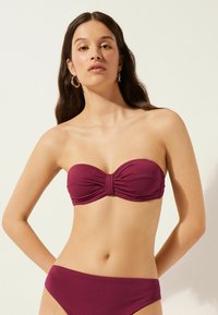 Ensemble de bikini bordeaux comprenant un haut bandeau texturé avec un détail de nœud et un bas taille basse assorti, mettant en avant un design lisse et ajusté.