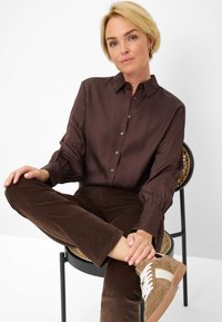 Bruine zijden blouse met manchet mouwen, gecombineerd met donkerbruine corduroypantalons en beige-bruin sneakers met witte accenten.