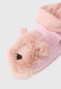 Roza obutev v obliki copat z nežnim medvedkom, ki ima ušesa in mehak material, ter zavihan rob. Dodatki vključujejo črne izšite oči in nos.