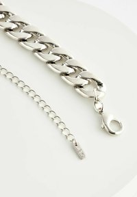 Bratara din metal argintiu cu un design gros și neted. Este securizată cu un închizător tip homar, având o secțiune ajustabilă a lanțului pentru lungime.