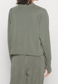 Sudadera de manga larga en tejido verde apagado con un corte holgado, que presenta un escote redondo, detalles cosidos y lazos laterales ajustables.