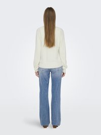 Cream sweater made from a soft, textured fabric paired with light blue, flared jeans featuring a faded wash and five-pocket design.