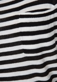 Gros plan d'un tissu rayé horizontal noir et blanc avec une petite ouverture de poche près du centre.